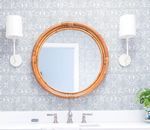 Round, wooden-framed mirror above a white sink with sconces; blue patterned wallpaper in the background.