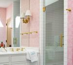 Pink and white bathroom with gold fixtures, glass shower, and patterned wallpaper.
