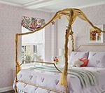 Bedroom with gold canopy bed, floral wallpaper, and patterned roman shade.