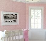 Pink wallpapered nursery with crib, framed artwork, and window with white trim.