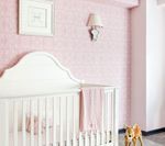 Pink nursery with white crib, framed art, wall sconce, and a toy deer.