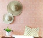 Two beige hats on a pink patterned wall above a shelf with a succulent, white fur, and a patterned pillow.