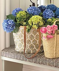 Two baskets filled with blue and green hydrangeas on a patterned surface. A small basket holds pink roses.