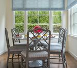 Dining room with round table, four chairs, window, blue shade, and exterior greenery.