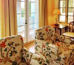 Two floral armchairs in a sunlit room with french doors and a side table.