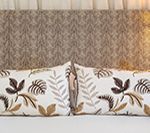Two pillows with leaf patterns on a bed, against a patterned headboard.