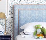 Blue patterned headboard with white linens, two frog plush toys, and speckled wallpaper.