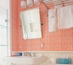 Bathroom with coral-colored tiled walls, mirror, sink, towels, and lights.