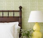 Brown bed headboard and a yellow lamp sit next to a pillow and a patterned green wall.