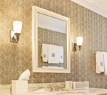 Bathroom vanity with mirror, sconces, and towels, on textured wallpaper.