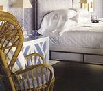 Wicker chair near a bed with white linens and a matching patterned nightstand.