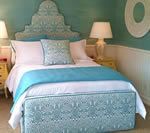 Bedroom with teal headboard, bedspread, and walls; white bedding; yellow nightstands; a wall decoration.
