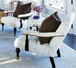 Two white patterned armchairs with brown pillows, small white table with flowers, light blue rug.