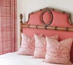 Coral-colored bedroom with bamboo-style headboard, patterned pillows, and matching curtains.
