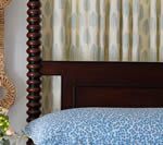 Dark wood bed with patterned blue bedding and light-colored patterned curtains.