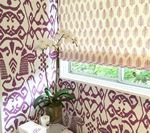 Purple patterned wallpaper and window shades with orchids on a counter.