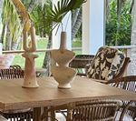 Wooden table set for dining, with decorative vases, rattan chairs, and tropical foliage background.