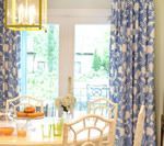 Dining room with blue floral curtains, white table and chairs, and a chandelier.