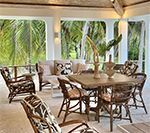 Outdoor seating area with rattan furniture, cushions, and lush greenery in the background.