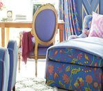 Blue floral chaise lounge and chair in a room with blue walls, floral curtains, and a desk.