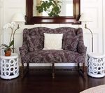 Couch with patterned fabric, flanked by white side tables and lamps, in front of a mirror.