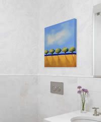 Blue and yellow abstract art of trees hanging on a wall in a bathroom, with a flower vase.