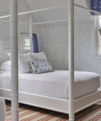 White canopy bed with white bedding, against a patterned wall, and a rug.