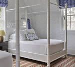 White canopy bed in a bright bedroom, with a striped rug and blue accents.
