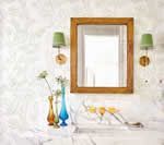 Mirror with wooden frame, sconces, and vases on a shelf against patterned wallpaper.