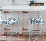Two clear acrylic bar stools with blue floral patterned seats in front of a white countertop.