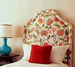 Bed with floral headboard, red pillow, blue lamp on a side table.