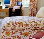 Bed with floral print, desk, chair, and curtains in a room with a window.