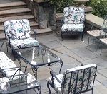 Patio furniture set: black metal frames, floral cushions, glass-top coffee table on stone patio.