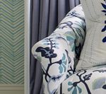 Close-up of a floral print armchair armrest with a blue and white design, next to blue curtains and patterned wallpaper.