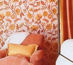 Coral armchair with yellow pillow, floral wallpaper, and orange curtain.