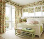Bedroom with floral curtains, wallpaper, and a white bed. A green bench sits at the foot of the bed.