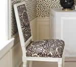 White chair with patterned seat and back, against a patterned wall.