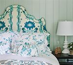 Bed with a patterned blue and white headboard and bedding, beside a bedside table with a lamp.