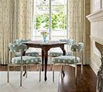 Dining area with round table, four chairs, and window with curtains; light blue, beige, and wood tones.