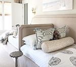 Bedroom with upholstered headboard, patterned bedding, decorative pillows, and small side table.