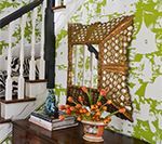 Wooden console table with mirror and floral arrangement against patterned wallpaper, near staircase.