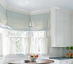 Kitchen with white cabinets, round table, fruit bowl, and light blue window shades.