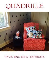 Red Quadrille chair in a room with a blue patterned wall, pillows and small chest.