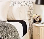 Bed with white bedding, black accent, polka dot headboard, and a bedside table with flowers.