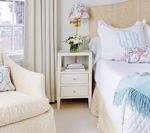 Bedroom with white furniture, floral lamp, blue accents, and a window with striped curtains.