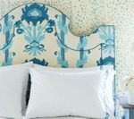 Blue patterned headboard with white pillows, on a bed, against a speckled wall.