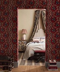 Bedroom framed in red floral wallpaper, bed with canopy, lamp on nightstand.