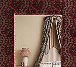 Mirror framed in patterned red fabric, reflecting a bedroom with patterned curtains and a lamp.