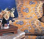 Couch with orange floral cushions, blue pillows, roses in a vase on a wooden table.
