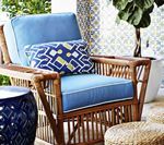 Rattan armchair with blue cushions and decorative pillow, on a patio setting with blue ceramic table.